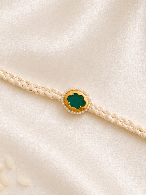 Green stone Rakhi with pearl detailing on an ivory braided thread, displayed on a silk background.