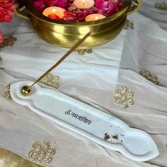 Incense stick with a brass bowl containing floating candles and rose petals on a decorative fabric.