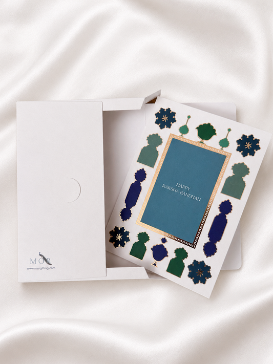 Premium Raksha Bandhan greeting card with blue and green foil accents and coordinating white gift box, designed to hold a greeting card and rakhi for elegant gifting.
