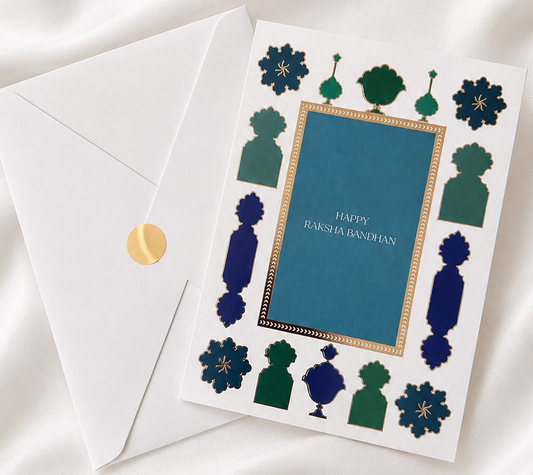 Premium Raksha Bandhan greeting card with blue and green gold foil accents and matching envelope, displayed on a white silk background.