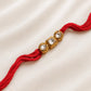 Three-Stone Kundan Rakhi with two round and one square bezel-set stones on a red thread, displayed on a silk background with rice.