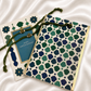 A Raksha Bandhan greeting card and matching envelope set arranged on a white satin fabric background. The envelope features a cream base with a repeating geometric trellis pattern in navy, teal, and green, finished with a gold border.