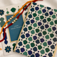 A festive Rakhi with a blue card and a patterned envelope on a white satin fabric background.