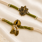 Bhai-Bhabhi Rakhi Set with an antique gold-tone Ganesha rakhi and Ghungroo bracelet with pearl and leaf accents on ivory and olive green threads, displayed on a silk background with kumkum and rice.