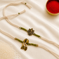 Bhai-Bhabhi Rakhi Set with an antique gold-tone Ganesha rakhi and Ghungroo bracelet with pearl and leaf accents on ivory and olive green threads, displayed on a silk background with kumkum and rice.