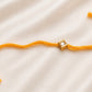 Single Square Kundan Rakhi with a bezel-set square stone on a yellow thread, displayed on a silk background.