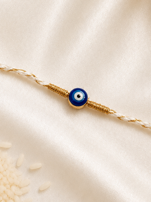 Blue evil eye Rakhi on a white braided thread with gold accents, displayed on a silk background.