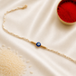 Blue evil eye Rakhi on a white braided thread with gold accents, displayed on a silk background with kumkum and rice.