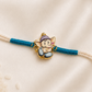 Kids Ganesha Rakhi with colorful enamel Lord Ganesha charm on a white thread with teal accents, displayed on a silk background.