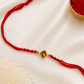 Gold-tone Ganesha Rakhi on a red thread, displayed on a silk background with kumkum and rice.
