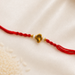 Gold-tone Ganesha Rakhi on a red thread, displayed on a silk background.