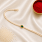 Green clover Rakhi with pearl detailing on an ivory braided thread, displayed on a silk background with kumkum and rice.