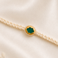 Green stone Rakhi with pearl detailing on an ivory braided thread, displayed on a silk background.