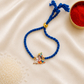 Kids Baby Krishna bracelet rakhi with adjustable blue braided cord and colorful enamel Krishna charm on a silk background.