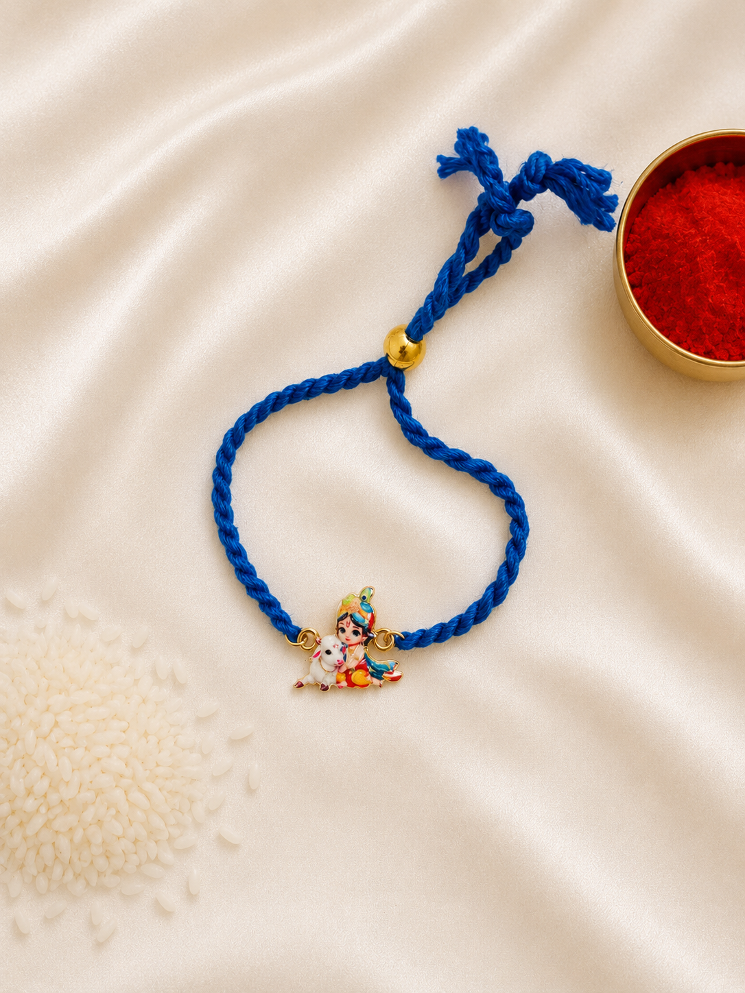 Kids Baby Krishna bracelet rakhi with adjustable blue braided cord and colorful enamel Krishna charm on a silk background.