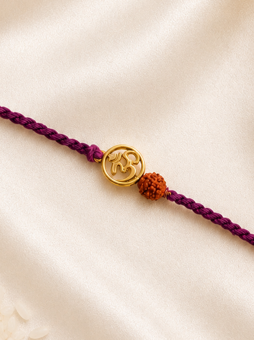 Gold-tone Om and Rudraksha Rakhi on a purple braided thread, displayed on a silk background.