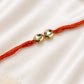 Twin Round Kundan Rakhi with two round bezel-set stones on a rust-orange thread, displayed on a silk background with kumkum and rice.