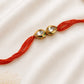 Twin Pear Kundan Rakhi with two pear-shaped bezel-set stones on a rust-orange thread, displayed on a silk background with kumkum and rice.