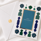 Premium Raksha Bandhan greeting card with blue and green gold foil accents and matching envelope, displayed on a white silk background.