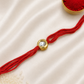 Single Round Kundan Rakhi with a bezel-set round stone on a red thread, displayed on a silk background with kumkum and rice.