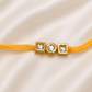 Triple Kundan Rakhi with round and square bezel-set stones on a yellow thread, displayed on a silk background