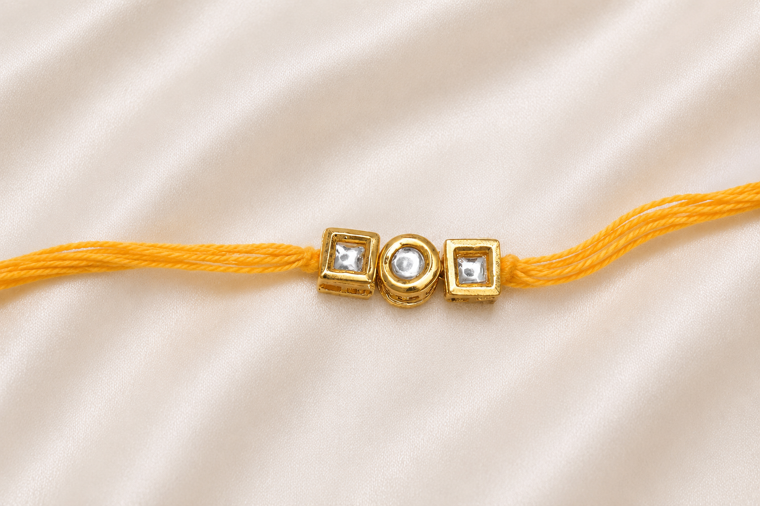 Triple Kundan Rakhi with round and square bezel-set stones on a yellow thread, displayed on a silk background