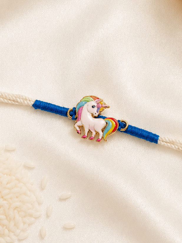 Kids Unicorn Rakhi with colorful enamel unicorn charm on a white thread with blue accents, displayed on a silk background.