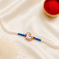 Kids Unicorn Rakhi with colorful enamel unicorn charm on a white thread with blue accents, displayed on a silk background with kumkum and rice.